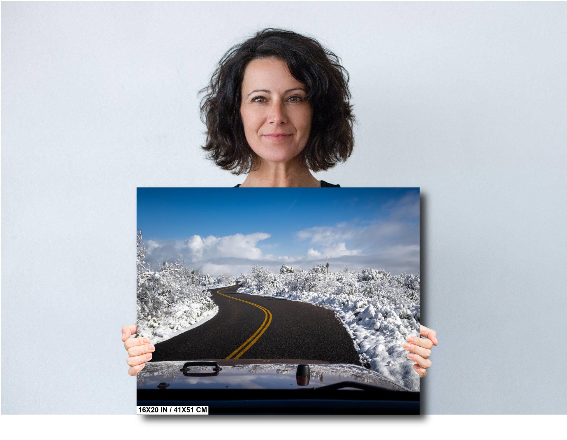 Snow-covered desert road in Saguaro National Park with cacti and a clear blue sky.