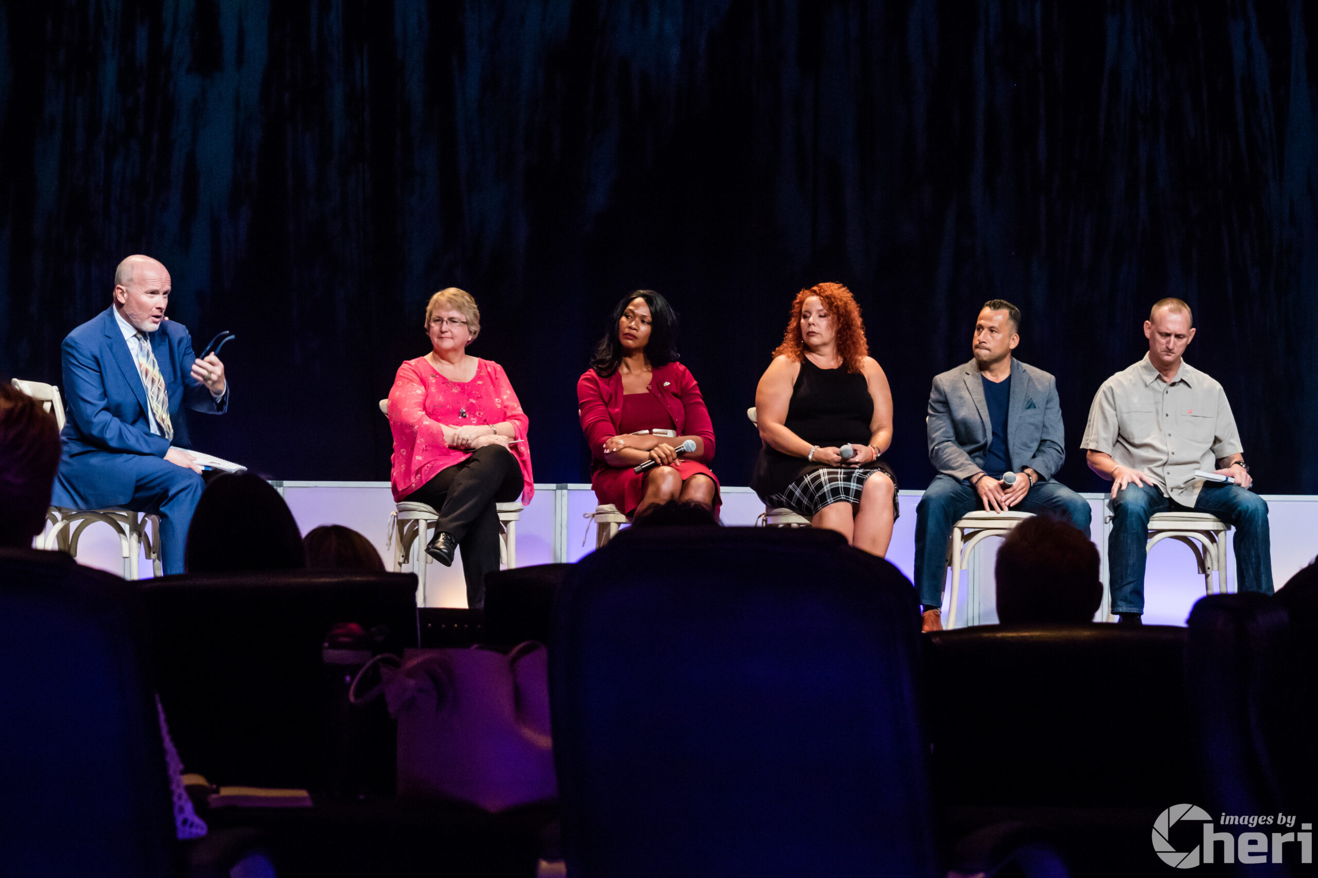 Corporate Panel Discussion Event Panel moderator in a blue suit speaking to five participants during a live Q&A session at a corporate event.