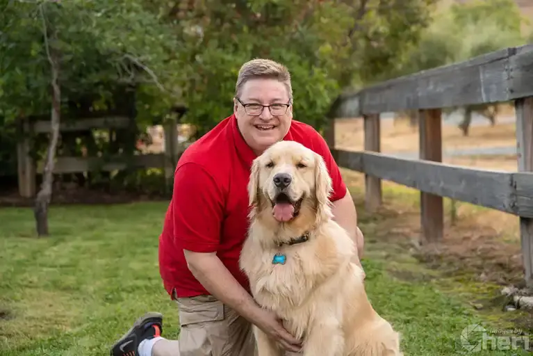 A man in a red shirt kneeling on the grass with his Golden Retriever during a 3-hour "Day-in-the-Life" pet photography experience.