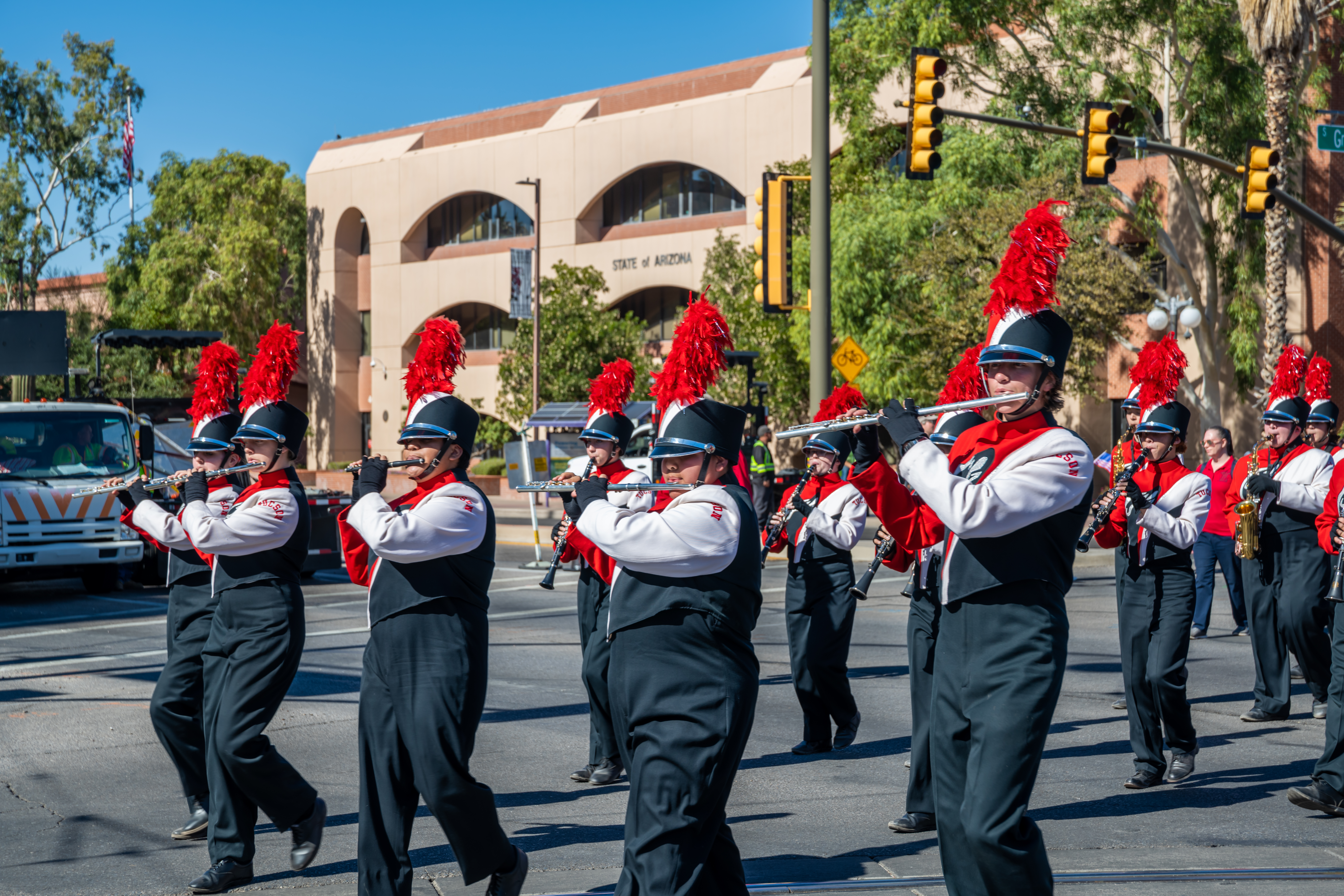 Tucson High Magnet School Marching Band Woodwinds Members of the Tucson High Magnet School marching band woodwind section, wearing white and black uniforms with red plumed shako hats, playing flutes and clarinets during a parade.