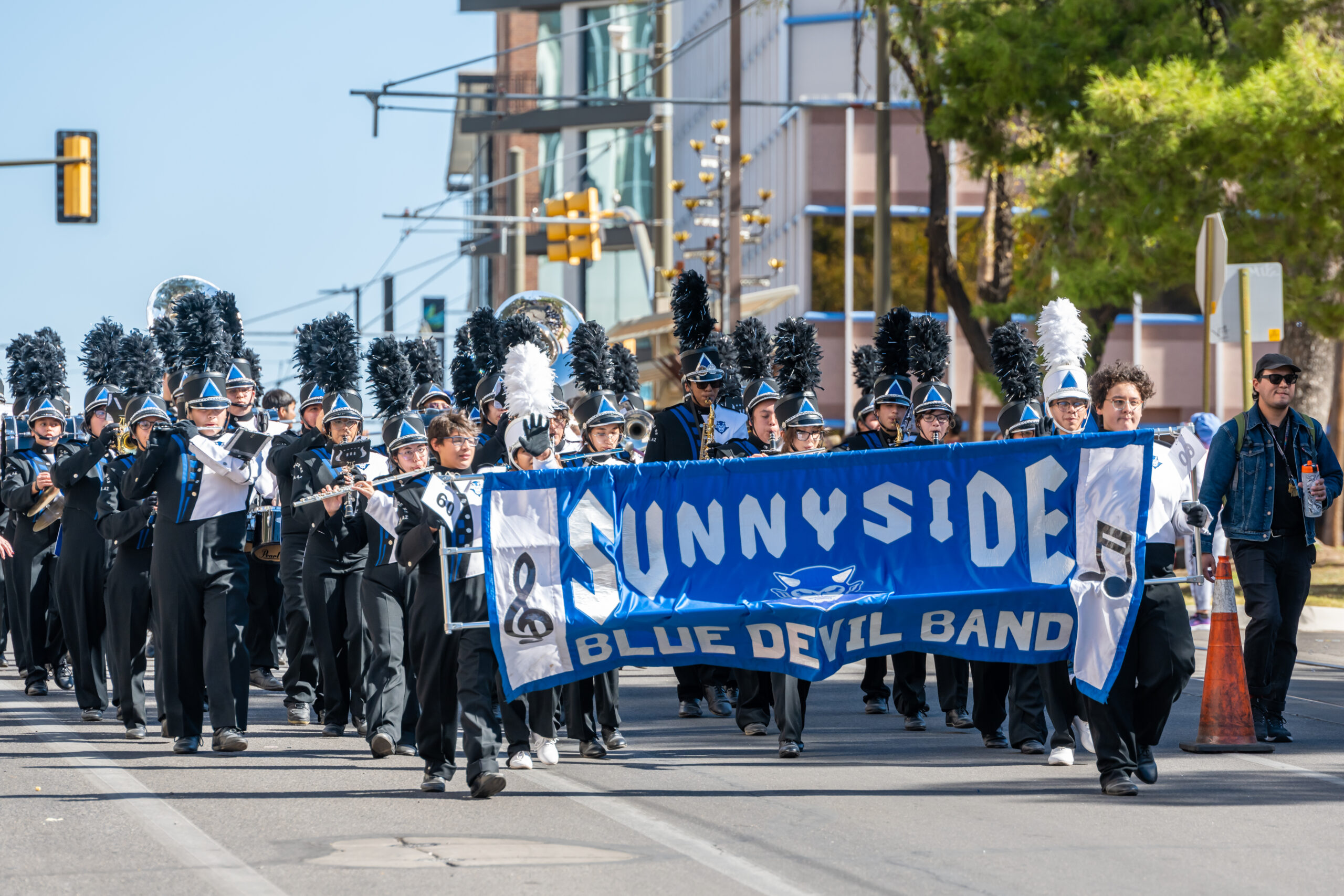 Sunnyside Blue Devil Band Parade Performance Sunnyside Blue Devil Band members in black and white uniforms with blue accents marching in a parade while playing brass and woodwind instruments.