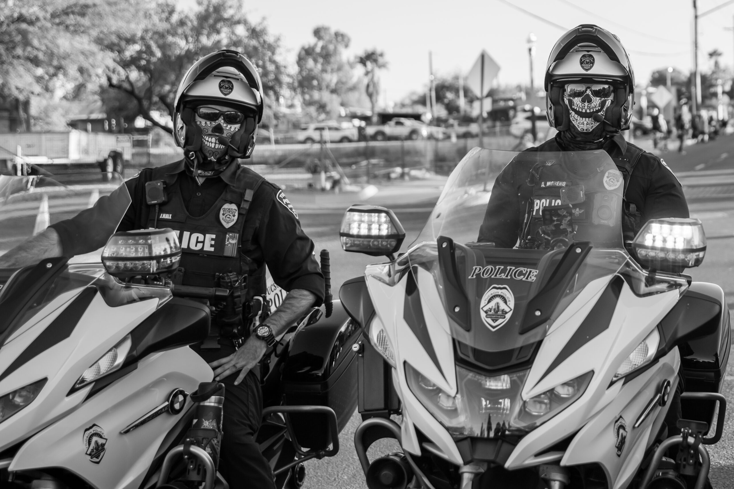 Police Officers in Skull Masks - Black and White Two motorcycle police officers wearing skull-patterned face masks and helmets while sitting on their patrol bikes.